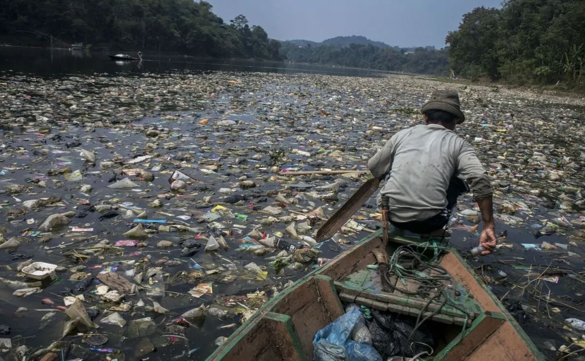 Seorang warga menggunakan perahu untuk melintasi Sungai Citarum yang penuh dengan sampah. Foto: Antara